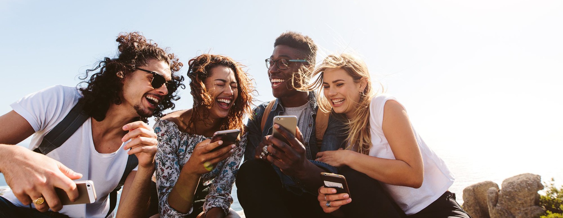 a group of friends sit outside laughing over their cell phones